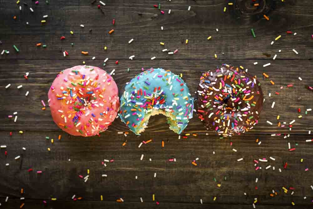 Three donuts with sprinkles on a wooden table, one is bitten