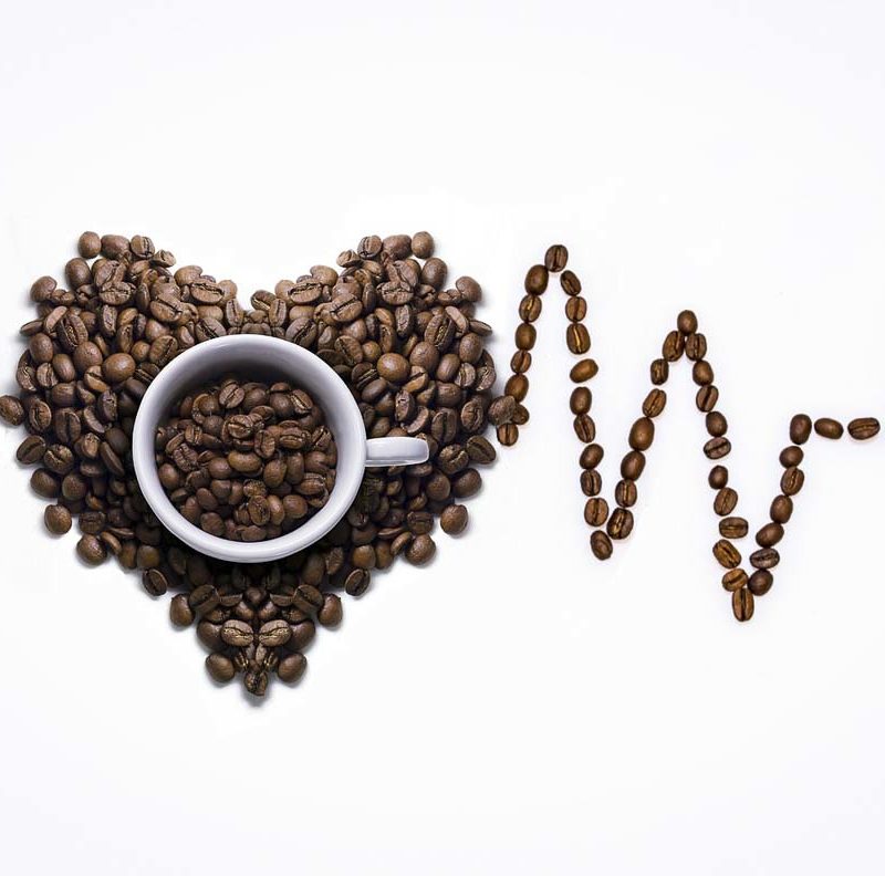 A cup with coffee beans with an Electrocardiagram made out of coffee beans