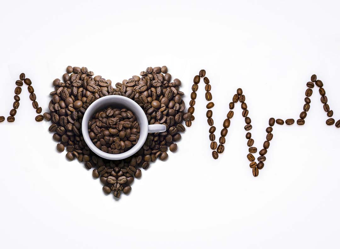 A cup with coffee beans with an Electrocardiagram made out of coffee beans